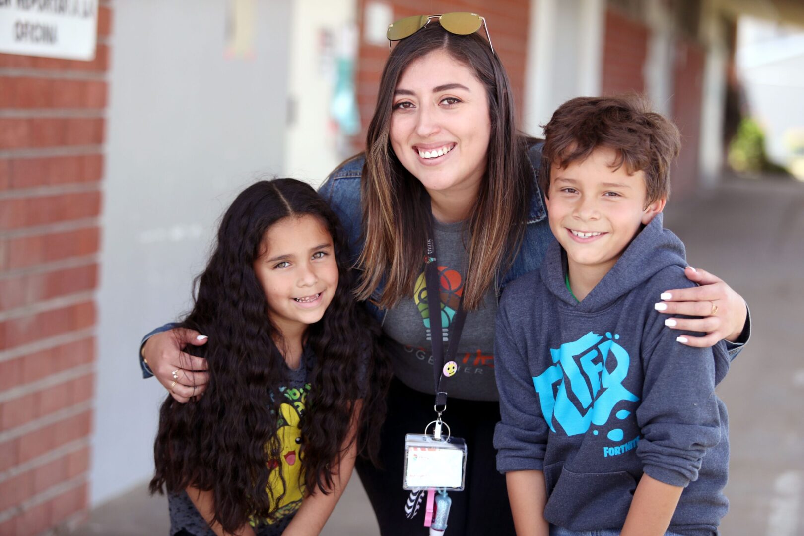A smiling instructor standing alongside a young boy and girl outside on a school campus.