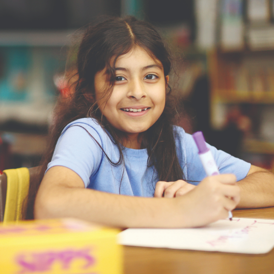 Student smiling while writing in class during a Think Together program.