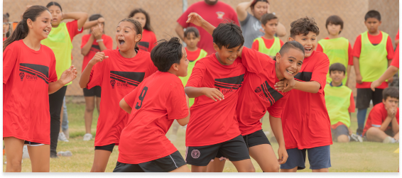 Kids in red jerseys celebrating during a Think Together soccer game.