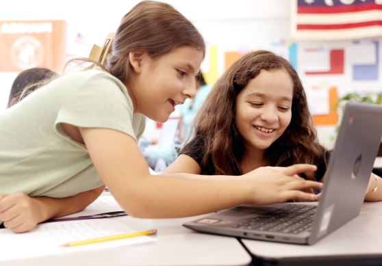 Two Think Together students smiling while collaborating on a laptop during class.